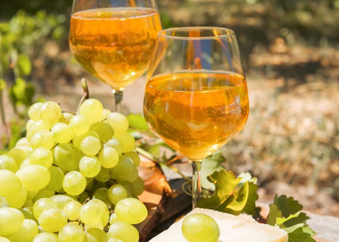 Beautiful still life with amber wine in glasses on the nature: a bright summer drink with cheese and grapes in a rustic style. Georgian national wine. Italian wine passito